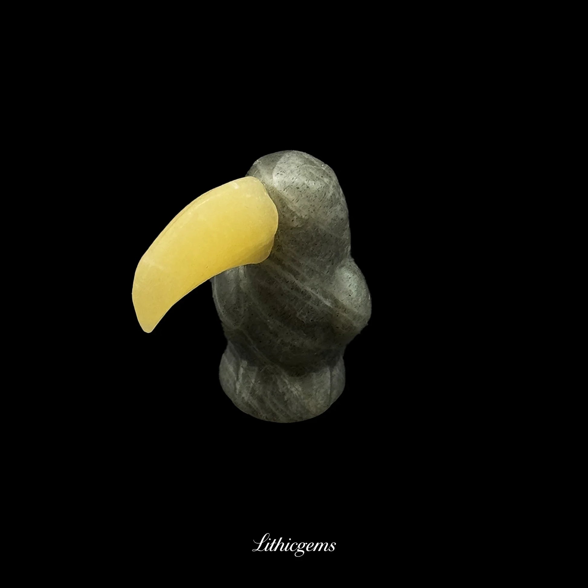 Hand-carved gemstone toucan figurine with yellow beak on black background, Lithicgems